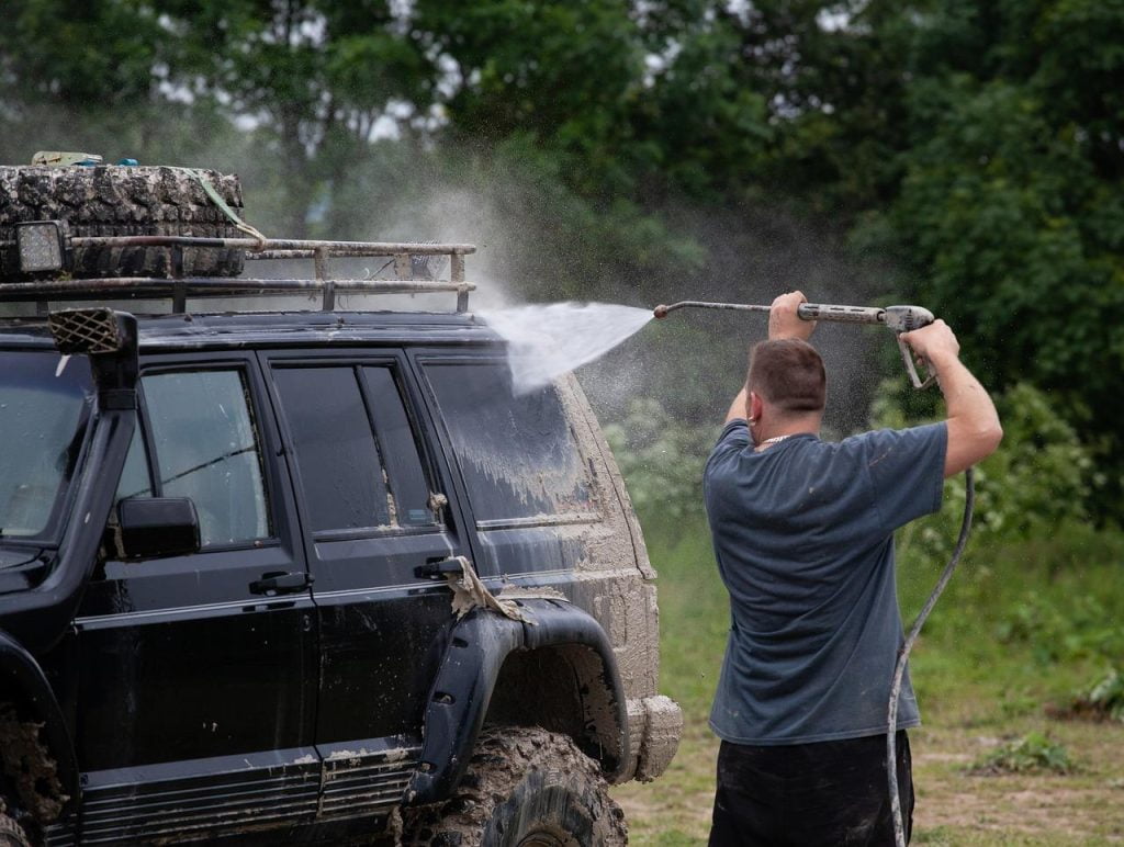 Man met een waterspuit om een auto te wassen in Amersfoort