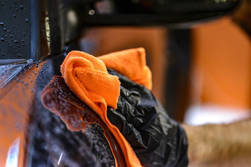 De hand van een man gebruikt een oranje doek om een ​​zwarte auto schoon te maken in Amersfoort